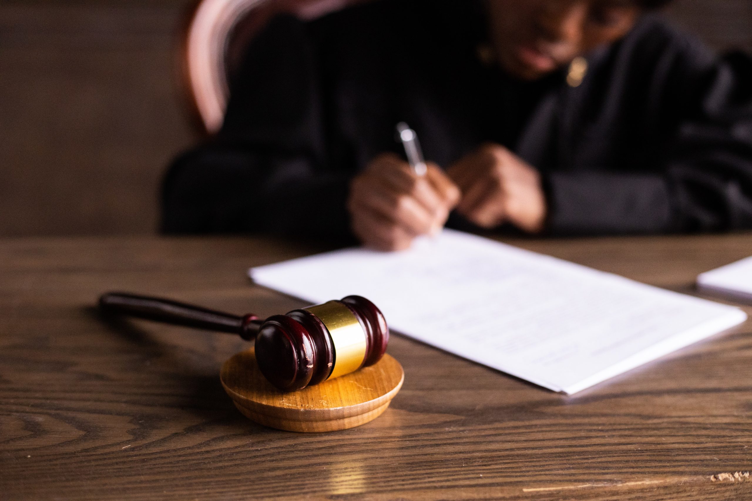 lawyer signing legal document next to wooden gavel resting on wooden table