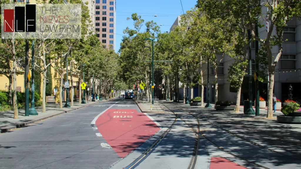 Tree-lined street with a red transit lane in downtown San Jose, with The Nieves Law Firm logo